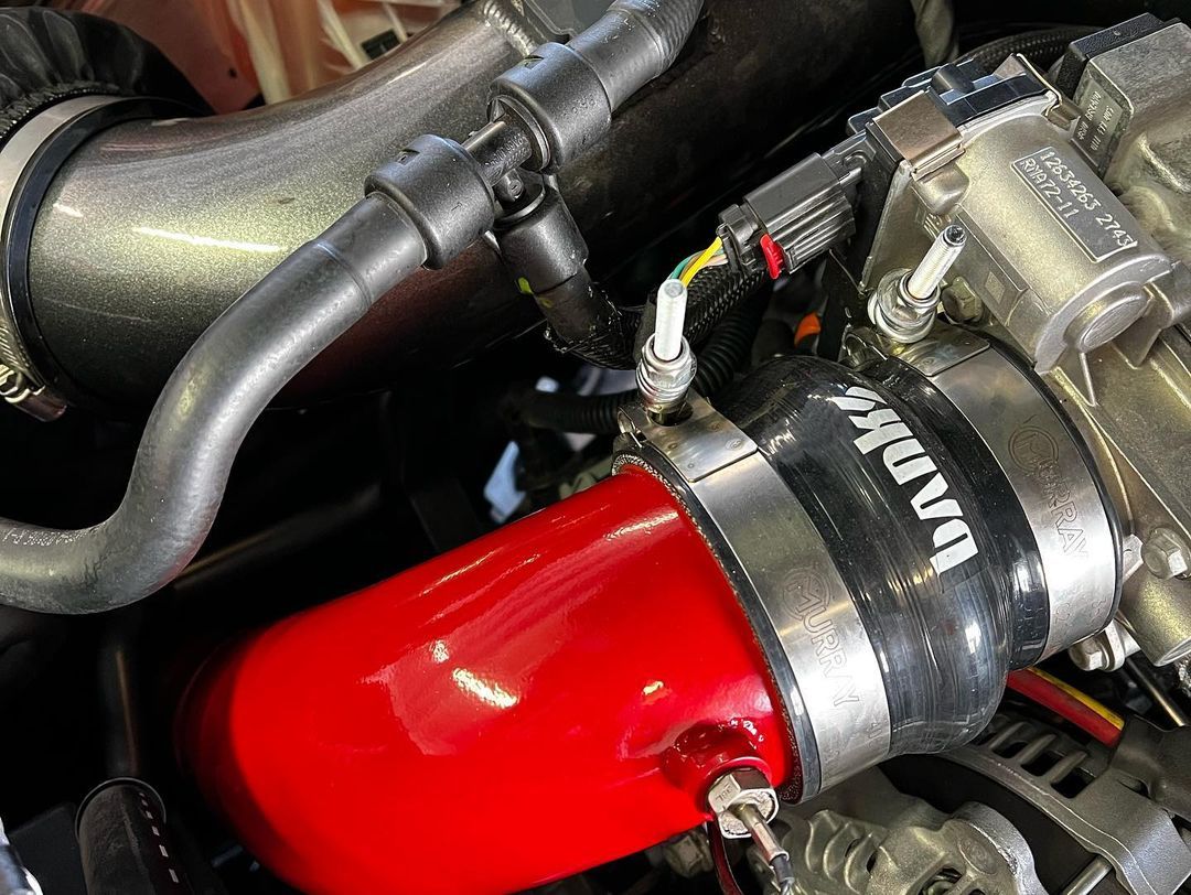 A close up of a car engine with a red hose attached to it.