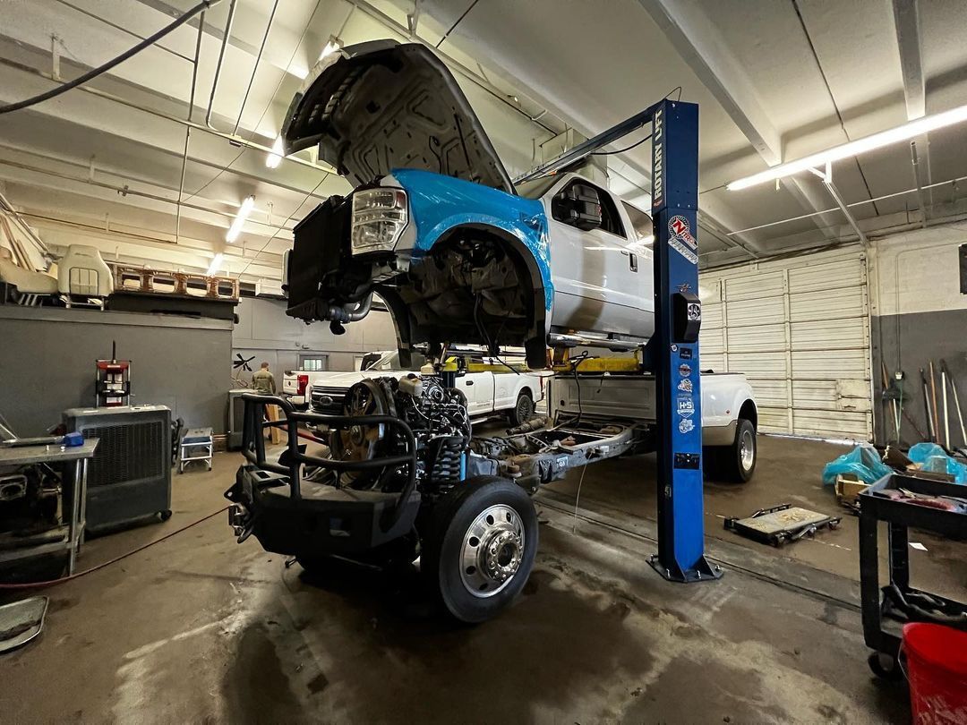 A truck is being worked on in a garage with the hood up.