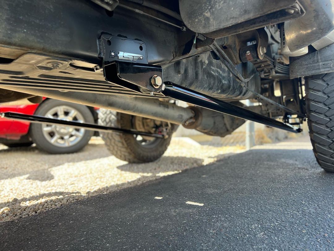 A close up of the underside of a truck with a red car in the background.