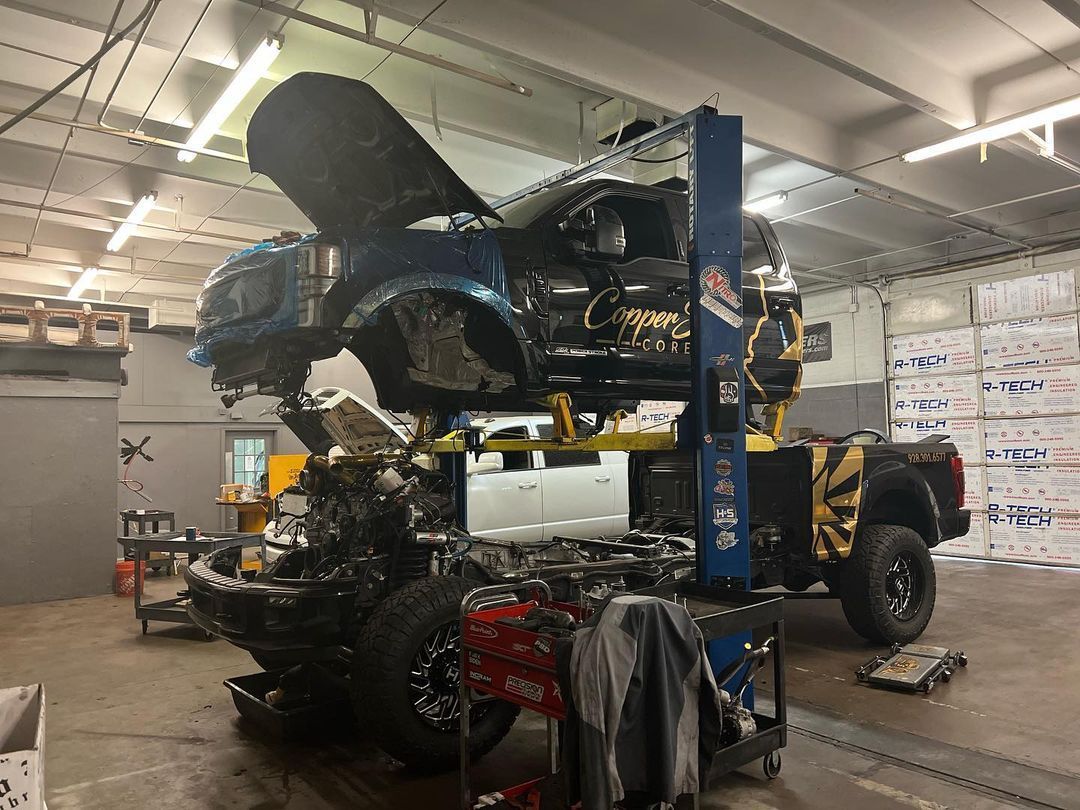 A car is being worked on in a garage with the hood up.
