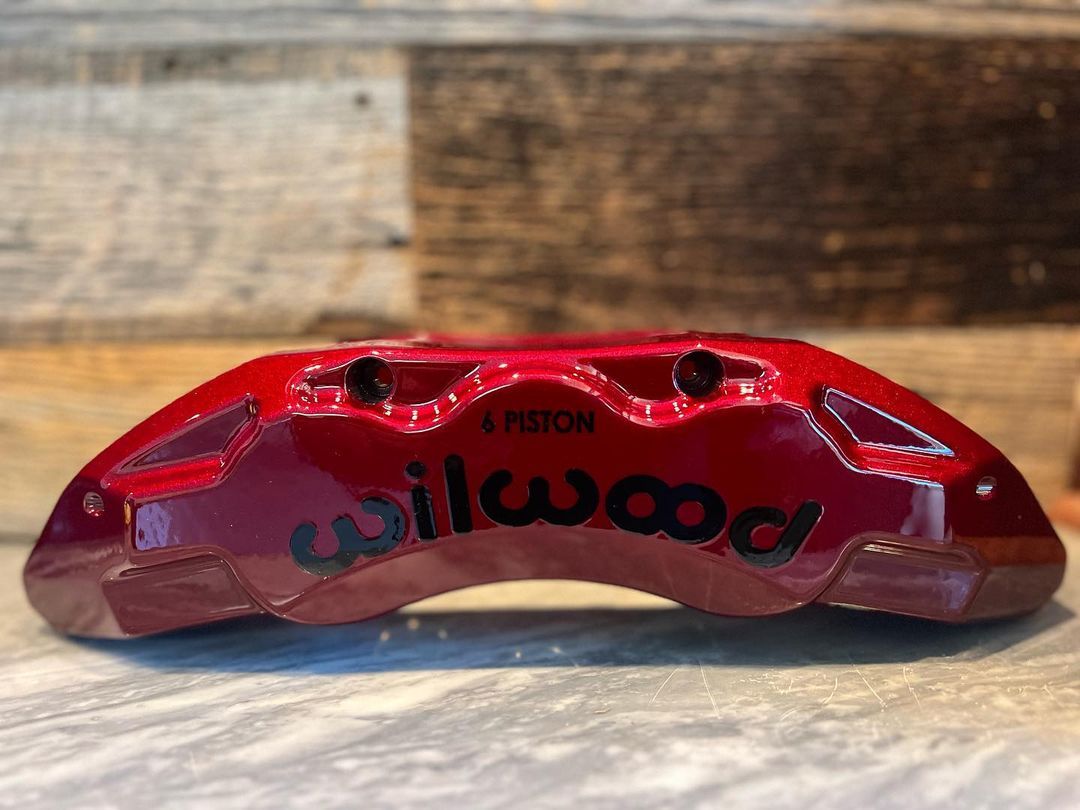 A red willwood brake caliper is sitting on a wooden table.