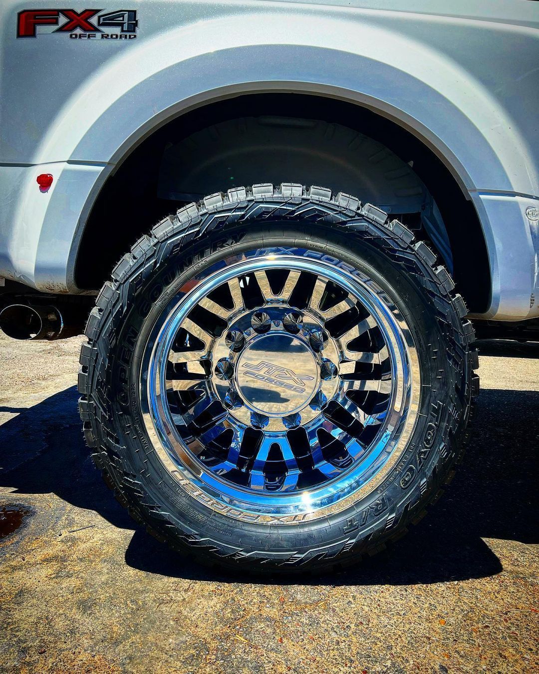 A silver truck with chrome wheels and tires is parked on the side of the road.