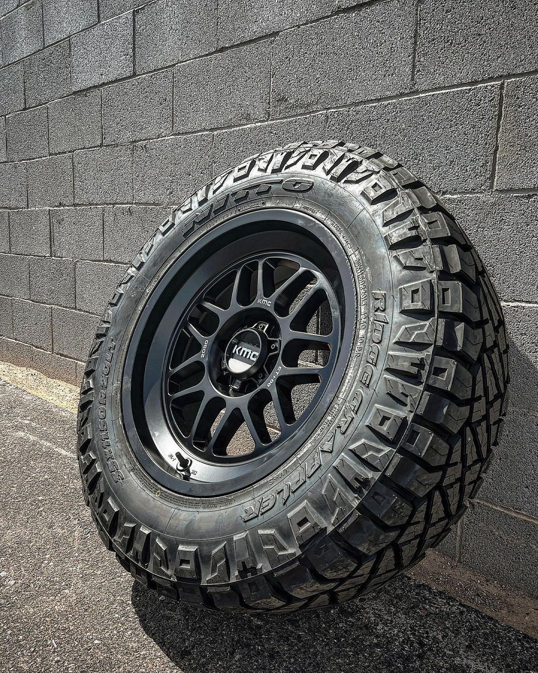 A tire is sitting on the ground in front of a brick wall.