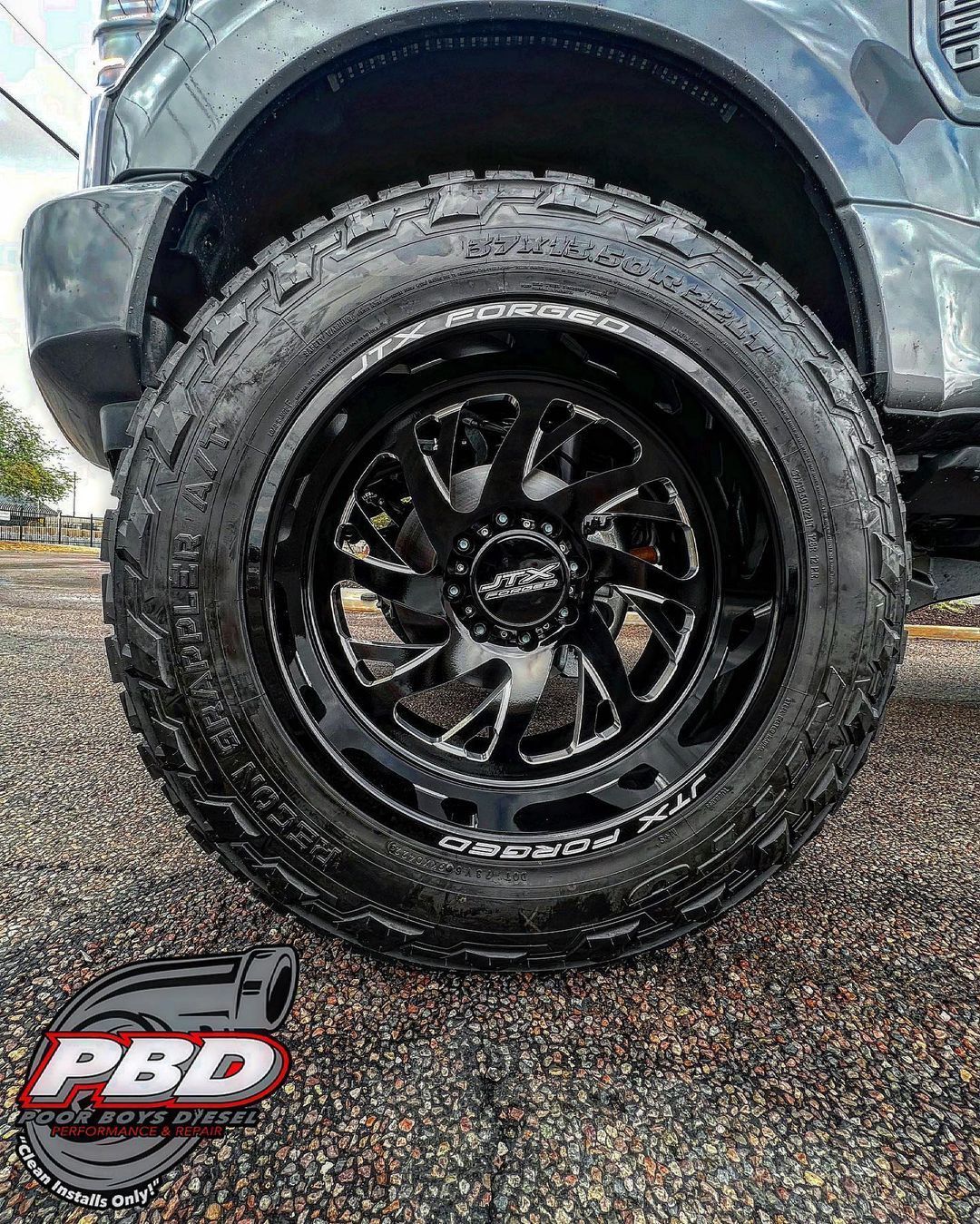 A close up of a truck wheel and tire on a gravel road.
