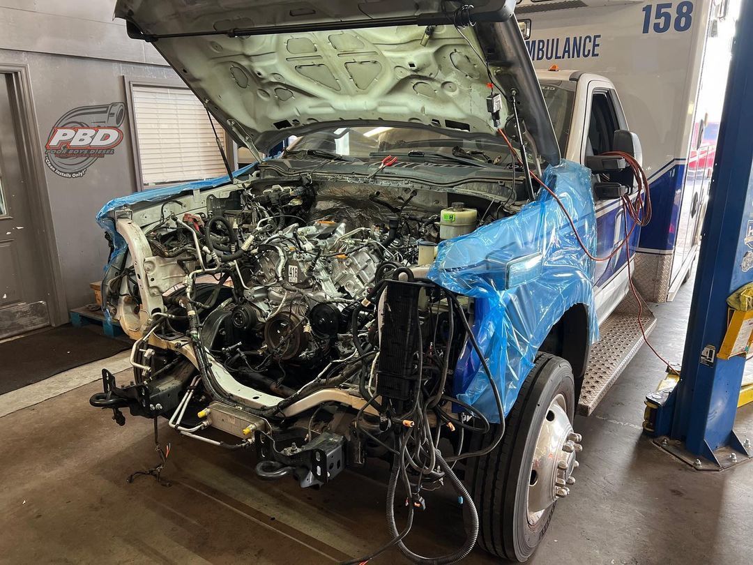 An ambulance with its hood up is sitting on a lift in a garage.