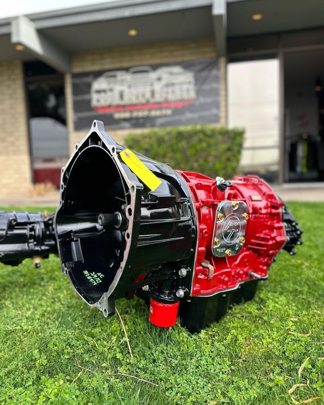 A red and black gearbox is sitting in the grass in front of a building.