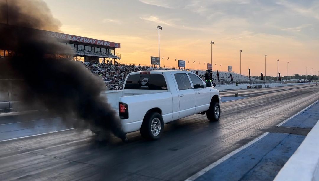 A white truck with black smoke coming out of it is driving down a race track.