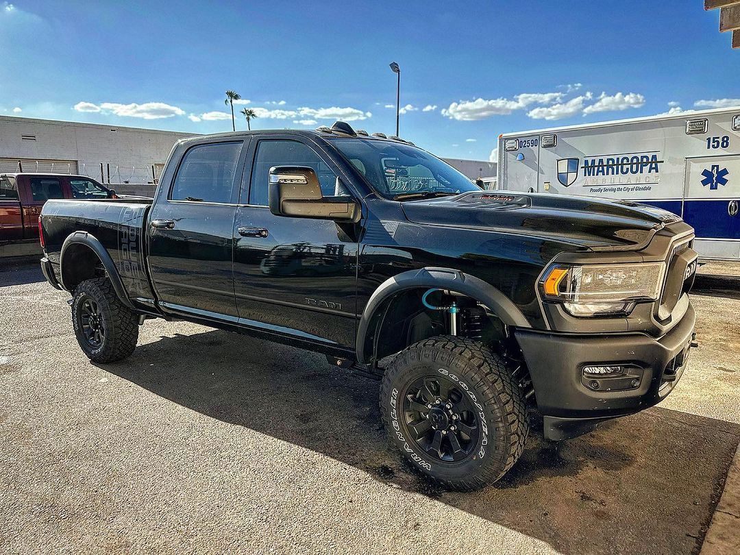 A black dodge ram truck is parked in a gravel lot next to a white ambulance.