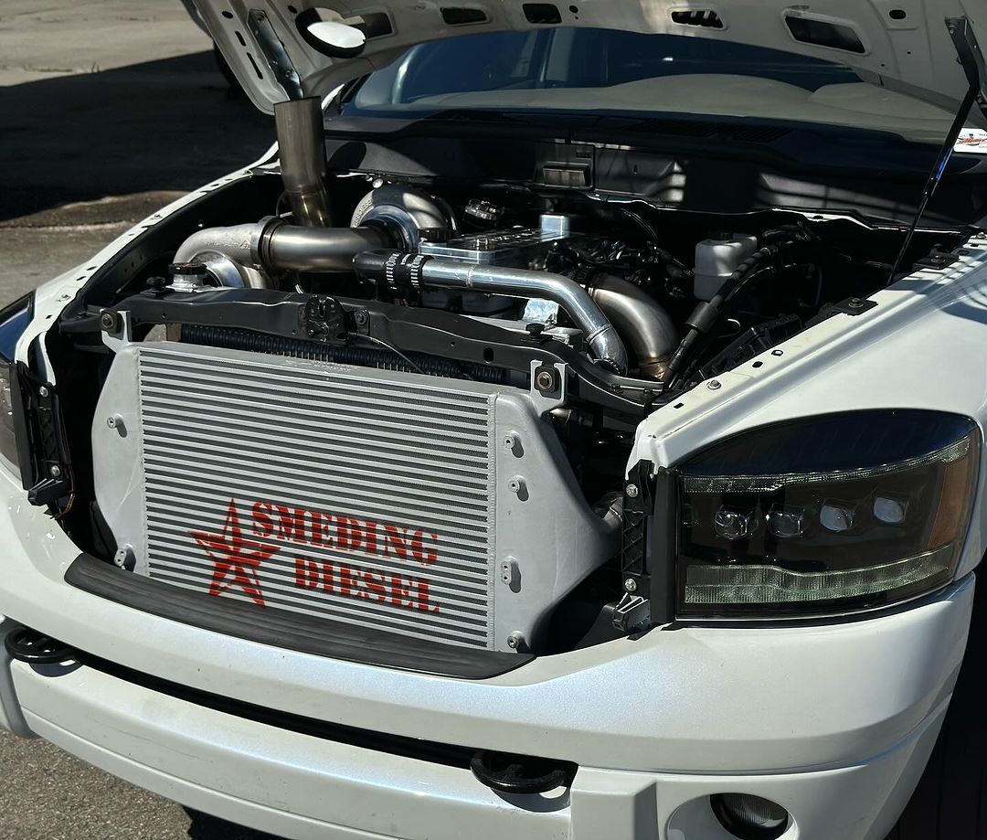 A white truck with the hood up has a radiator on the front