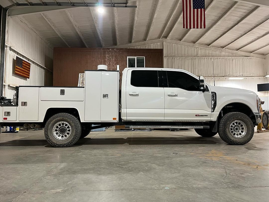 A white truck with a utility bed is parked in a garage.