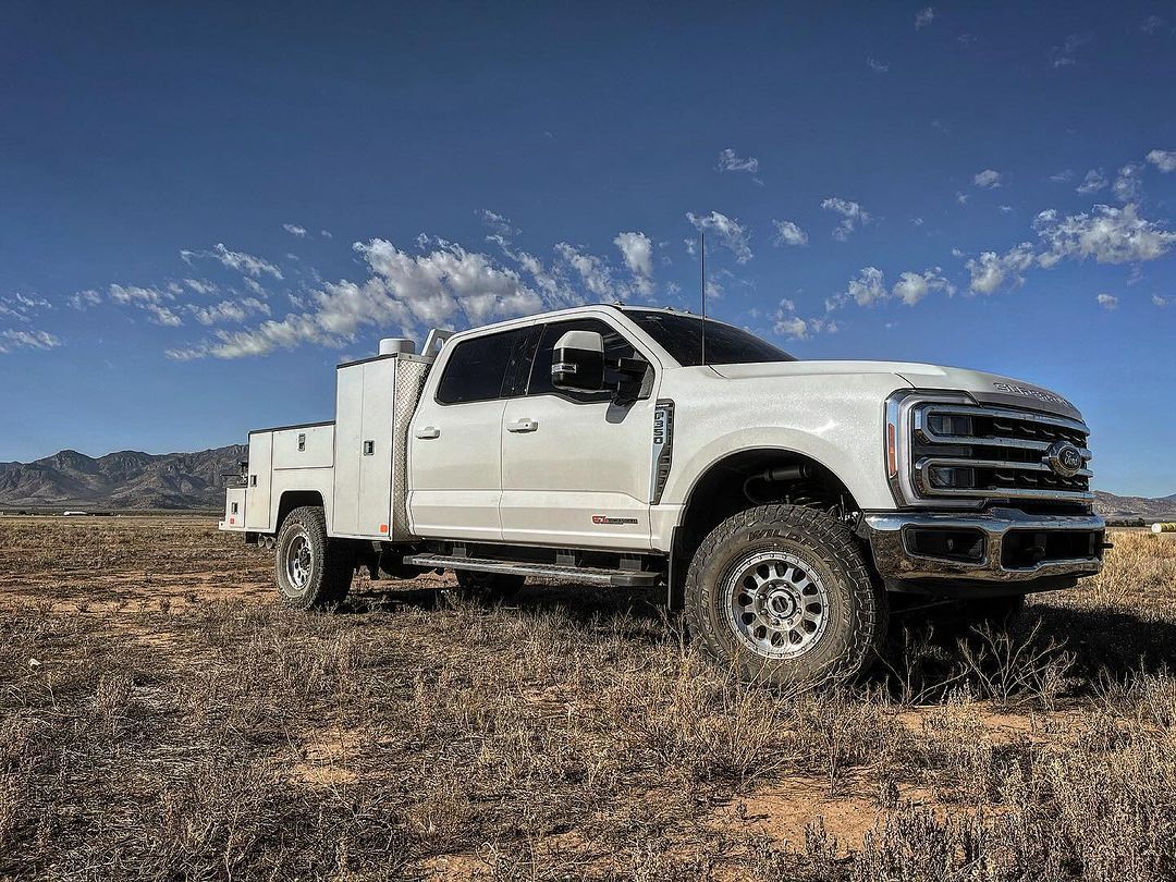 A white truck is parked in a dry grass field.