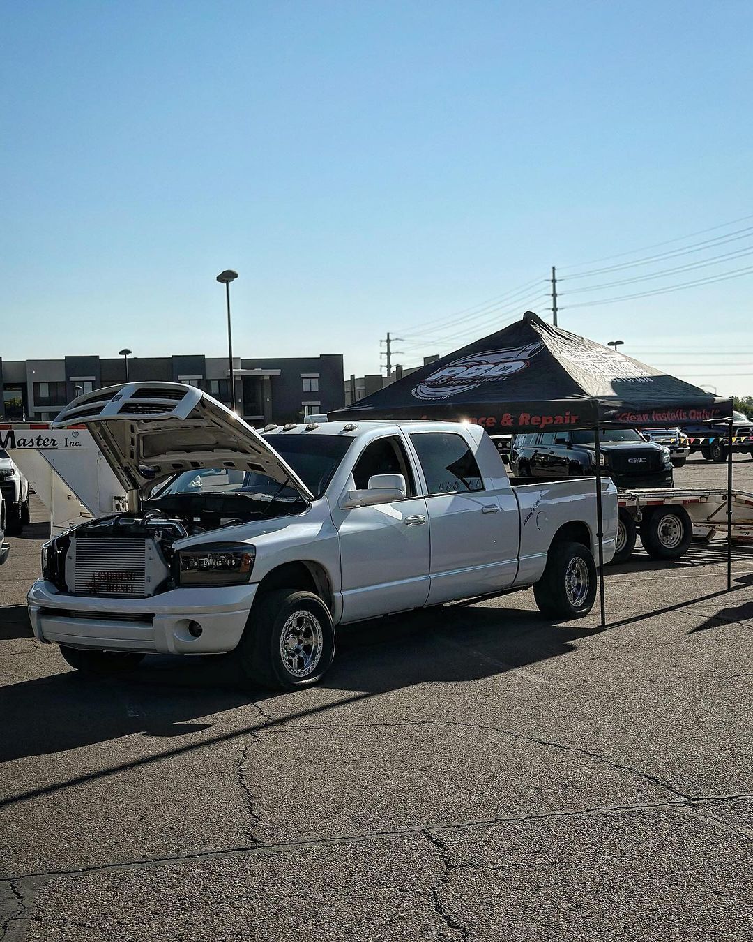 A white truck with the hood up is parked in a parking lot.