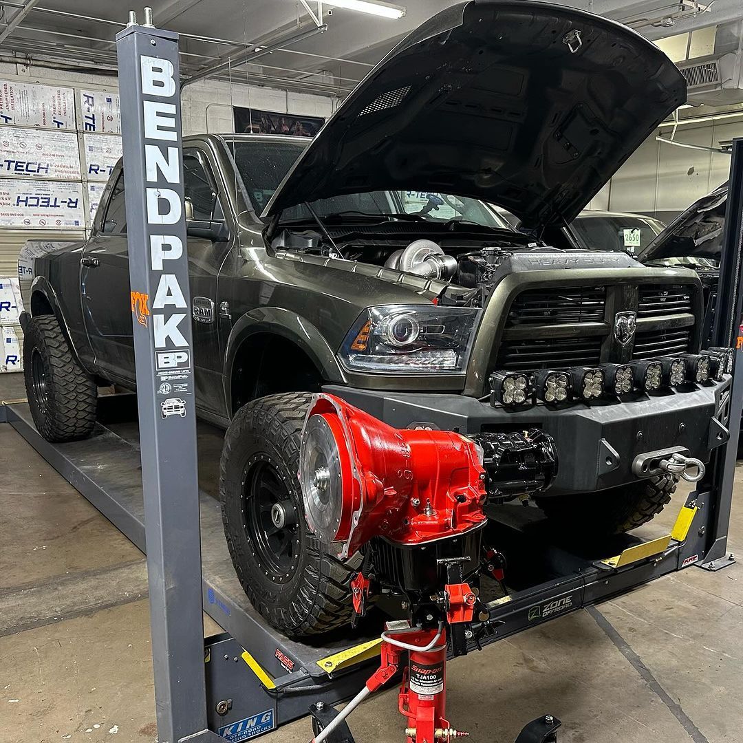 A truck with the hood up is on a lift in a garage.