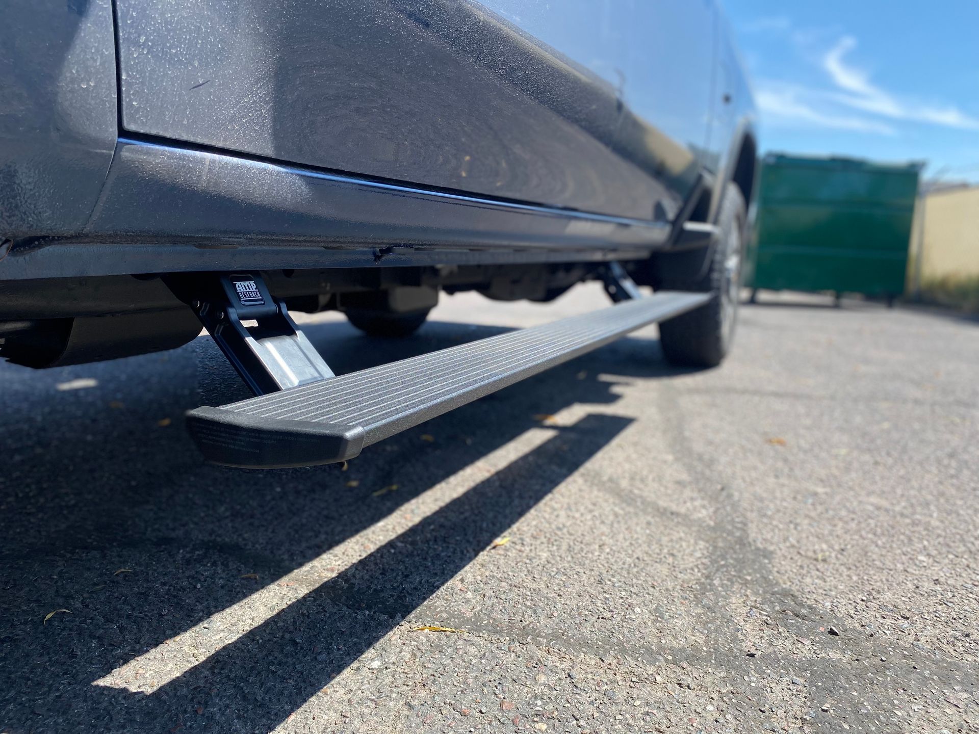 A gray truck with a side step is parked on the side of the road.