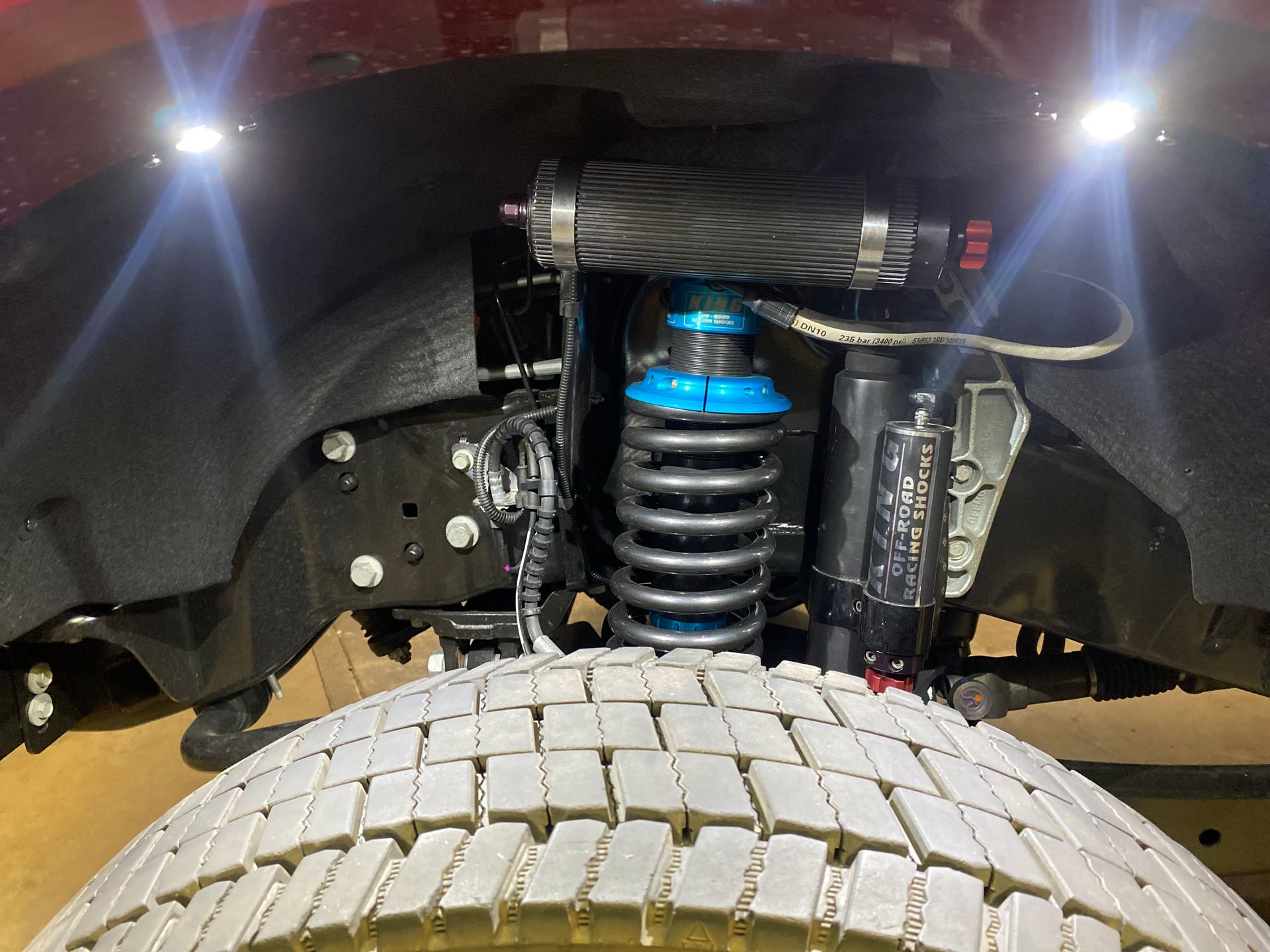 A close up of the underside of a truck with shocks and a tire.