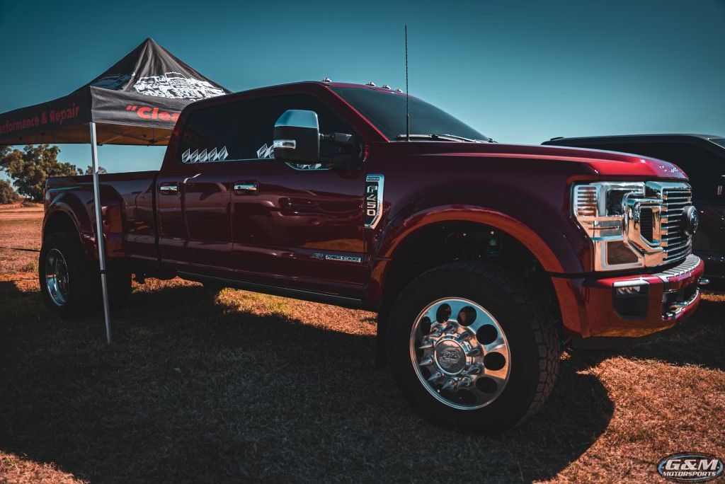 A red truck is parked under a tent in a field.
