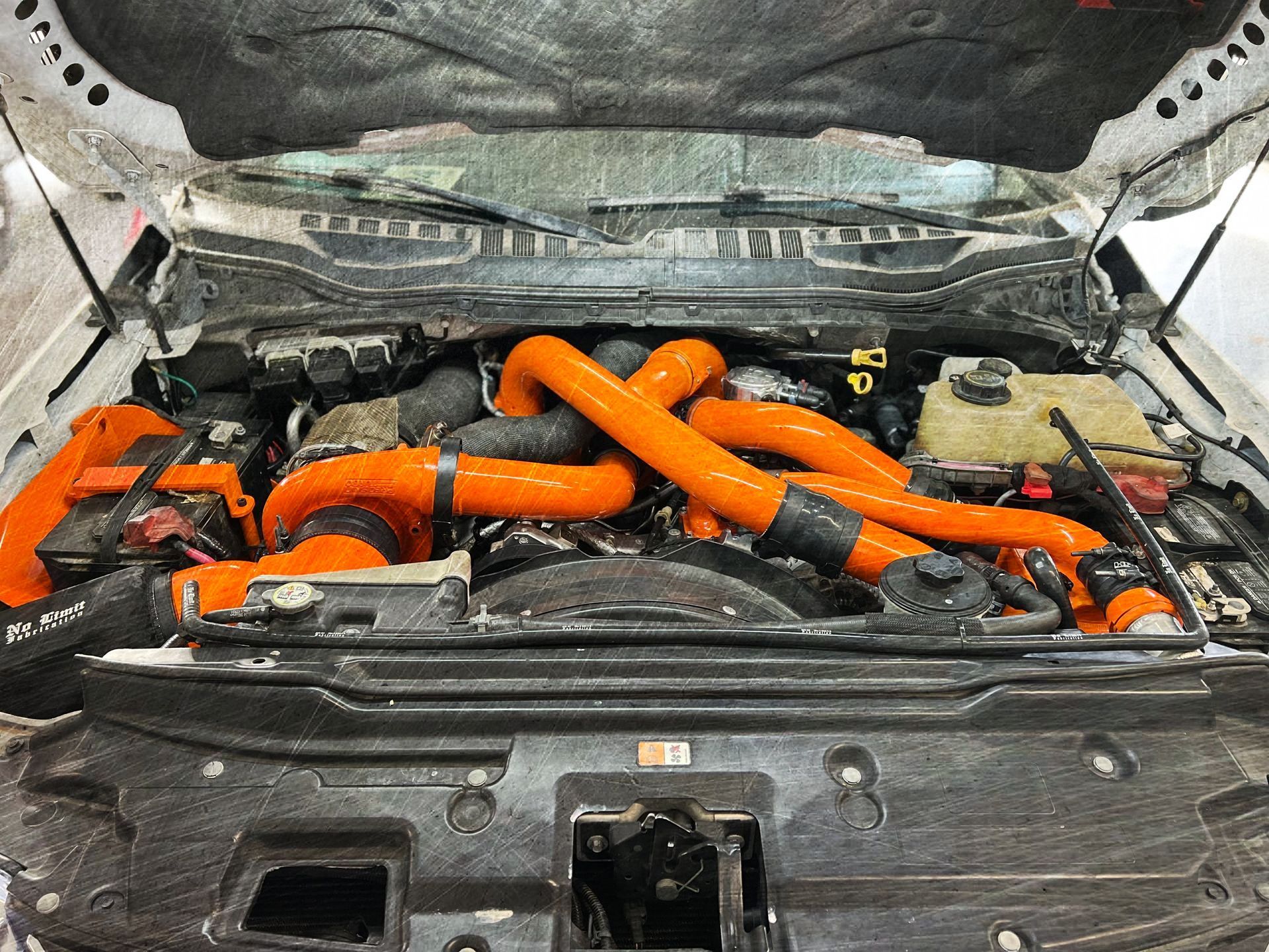 The engine of a white truck with the hood open and orange hoses coming out of it.