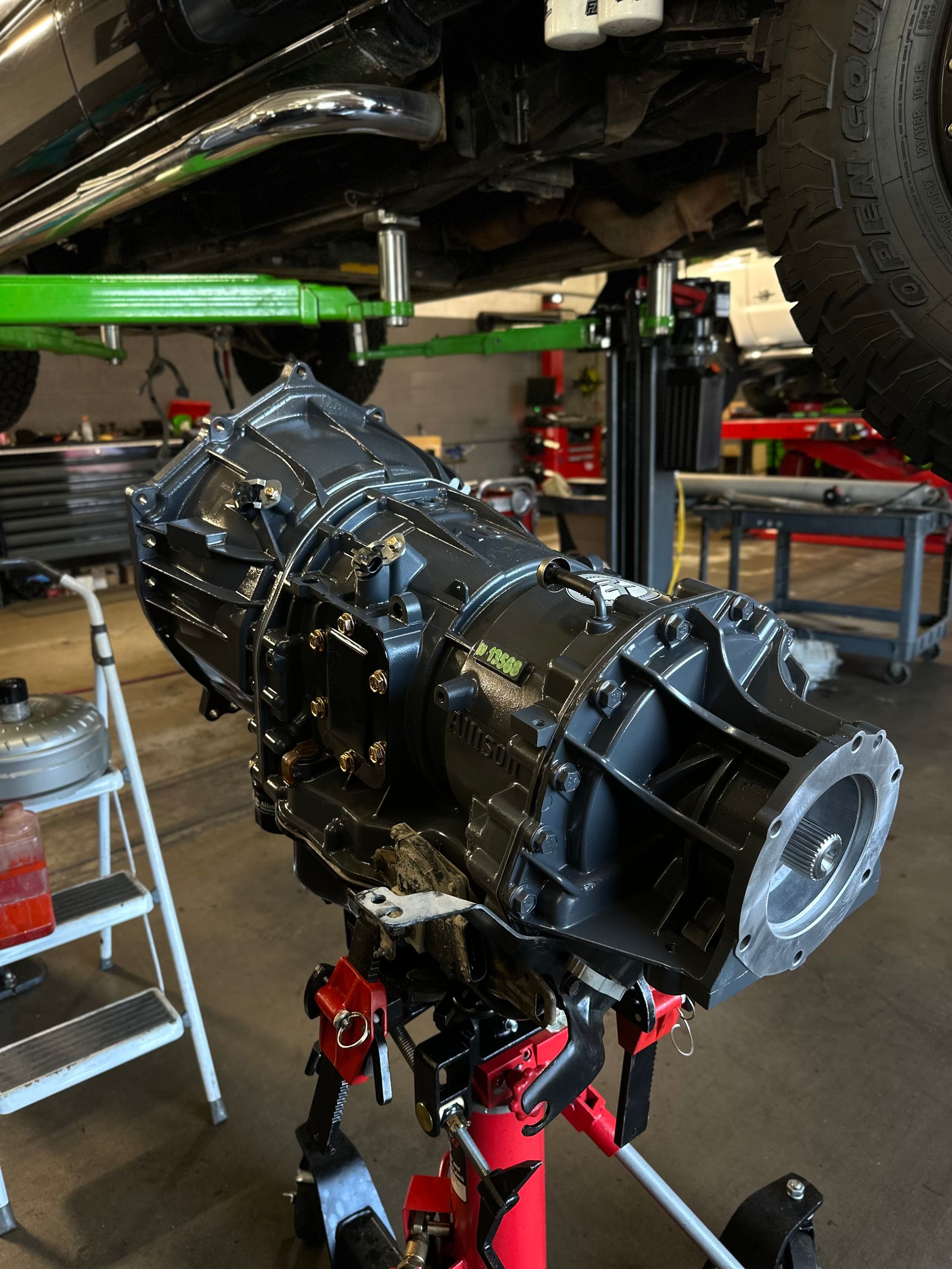 A gearbox is sitting on a stand under a car in a garage.