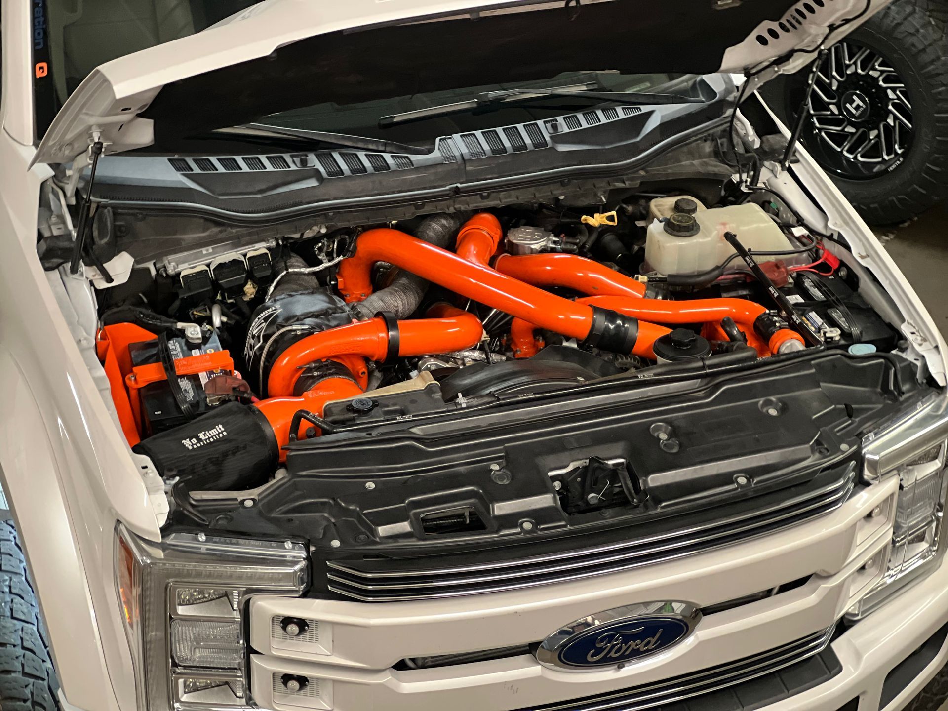 The hood of a white ford truck with orange hoses coming out of it.