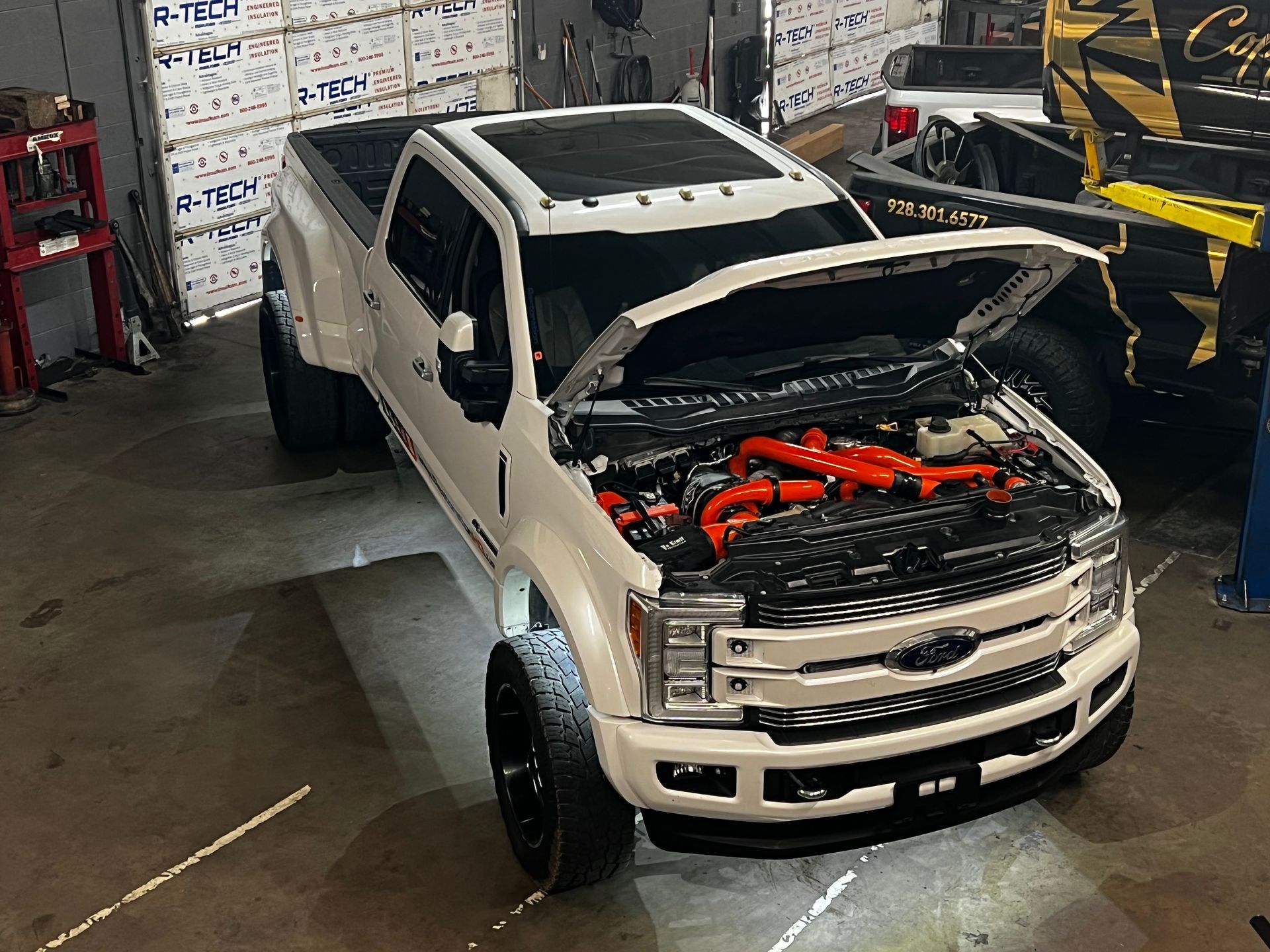 A white truck with the hood up is parked in a garage.