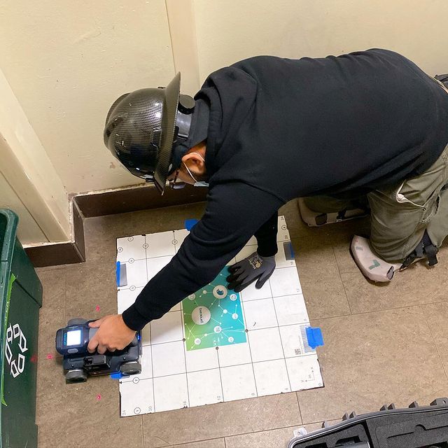 A man wearing a helmet is playing with a toy car on a tiled floor