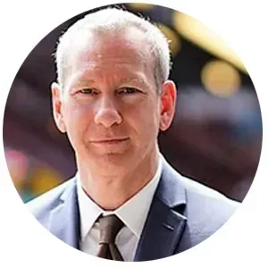 Man in a blue suit and brown tie, smiling slightly, outdoors.