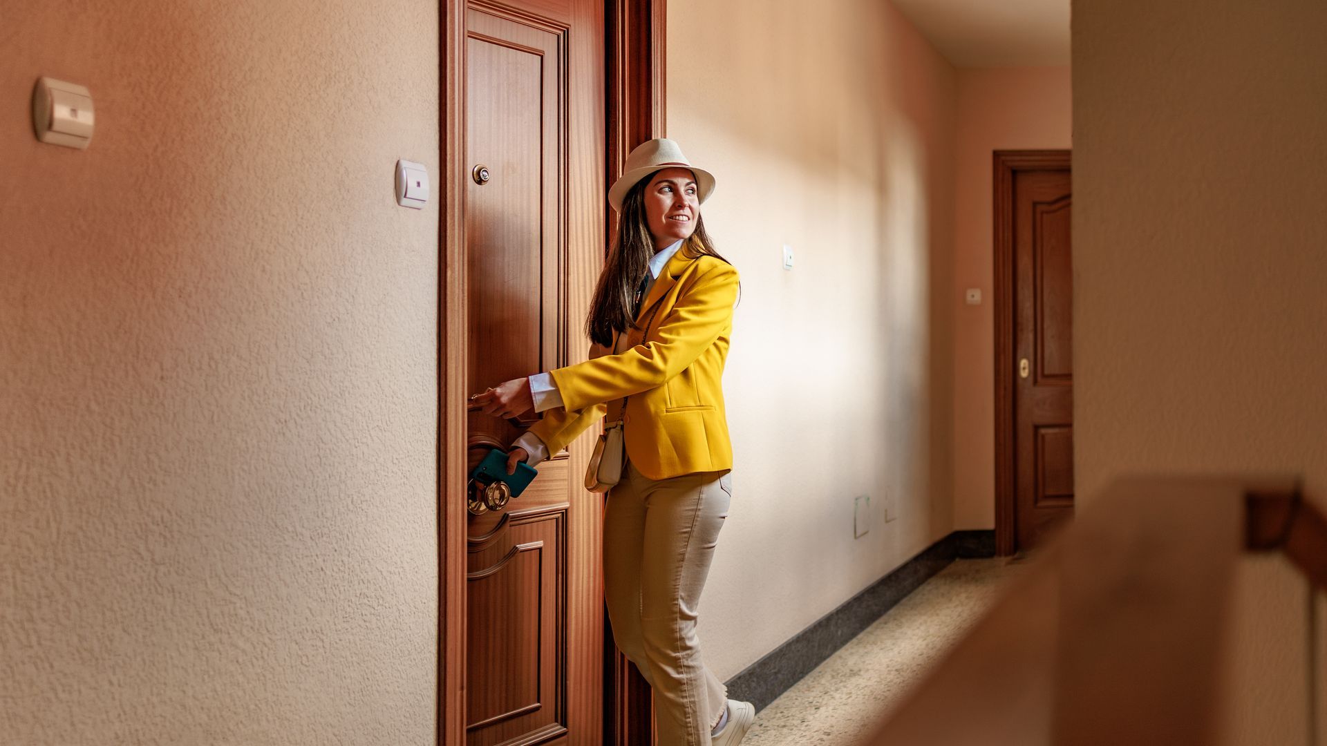 Woman in yellow jacket opening a wooden door in a hallway.