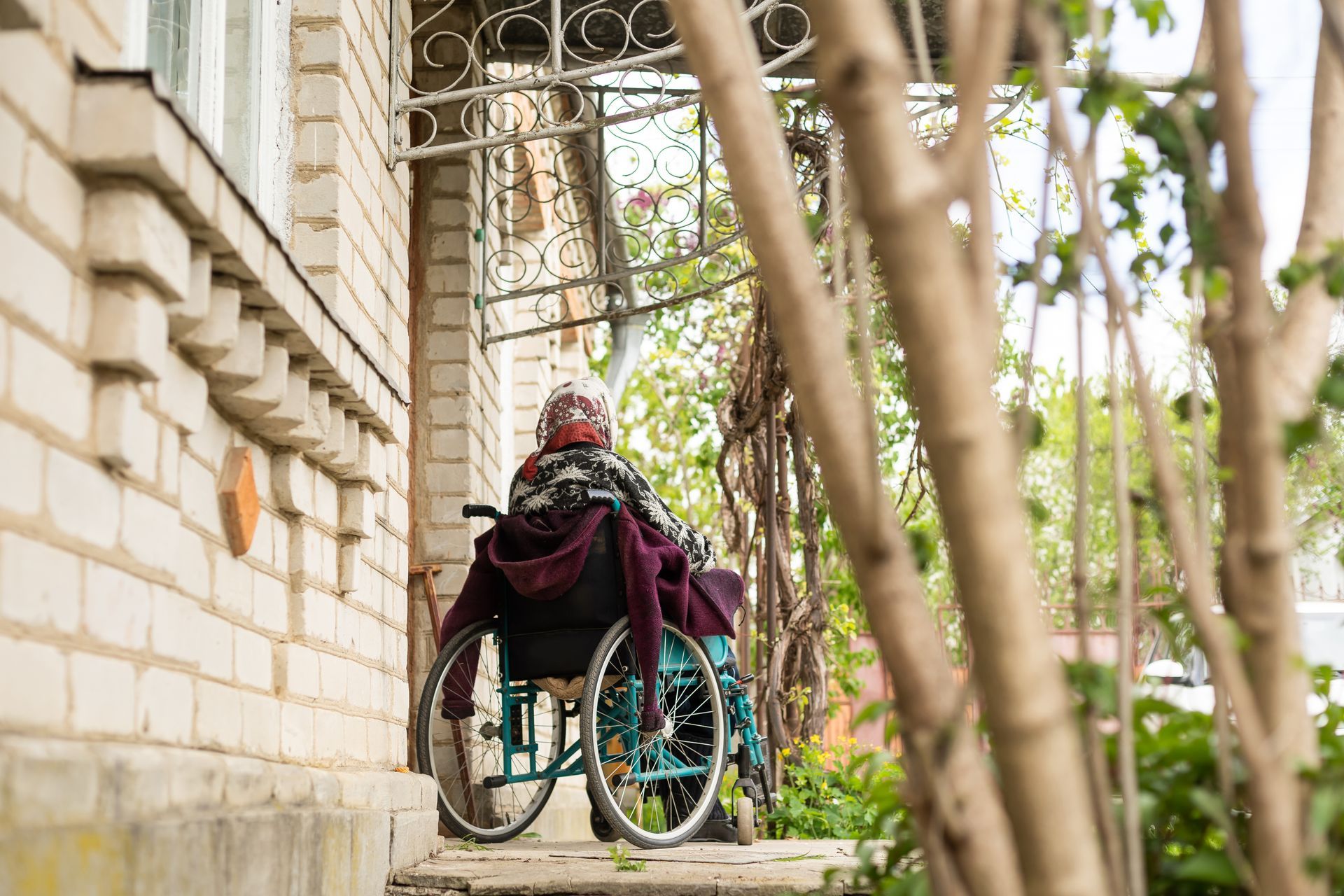 Person in a wheelchair at the doorway of a brick building with a decorative iron railing.