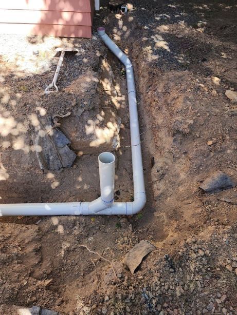 A White Pipe Is Laying In The Dirt Next To A House —  RAW Plumbing & Gasfitting In Pearce, ACT