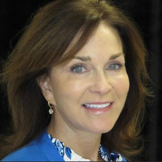 A woman wearing a blue shirt and earrings smiles for the camera