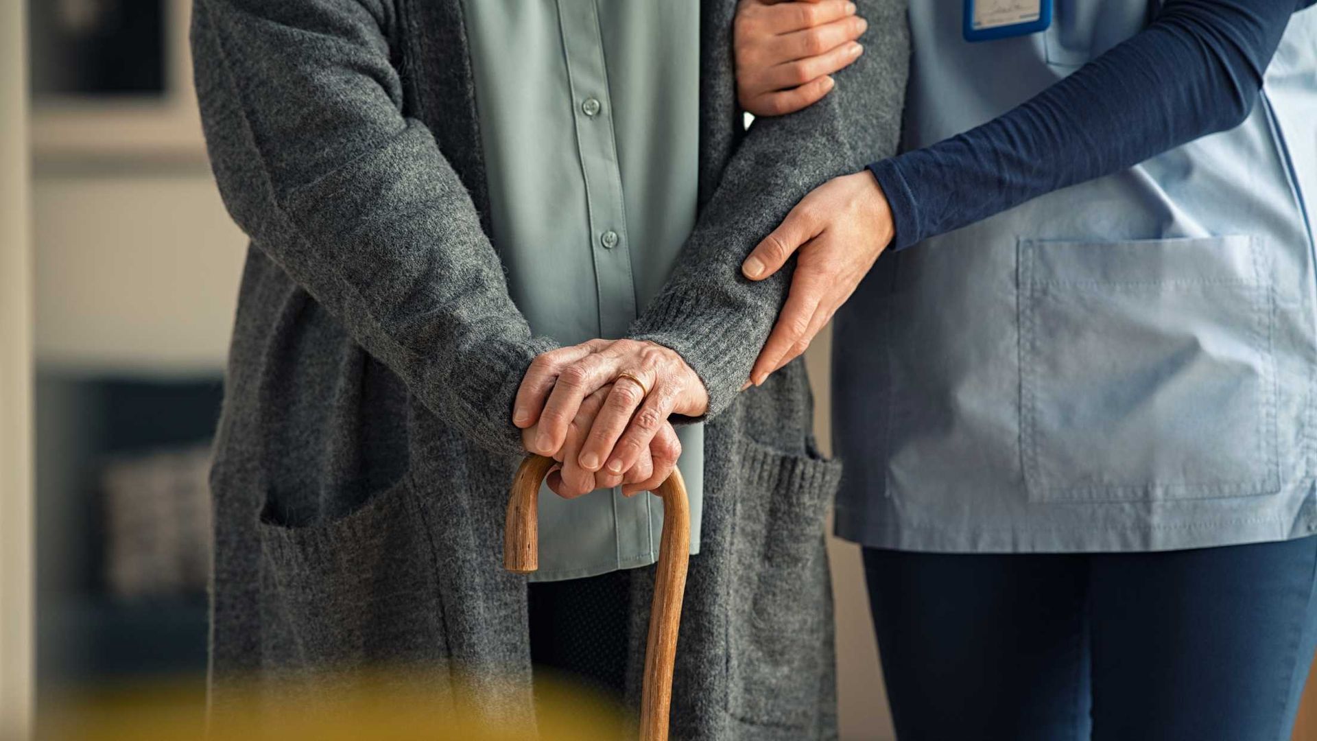 A nurse is helping an elderly woman with a cane.