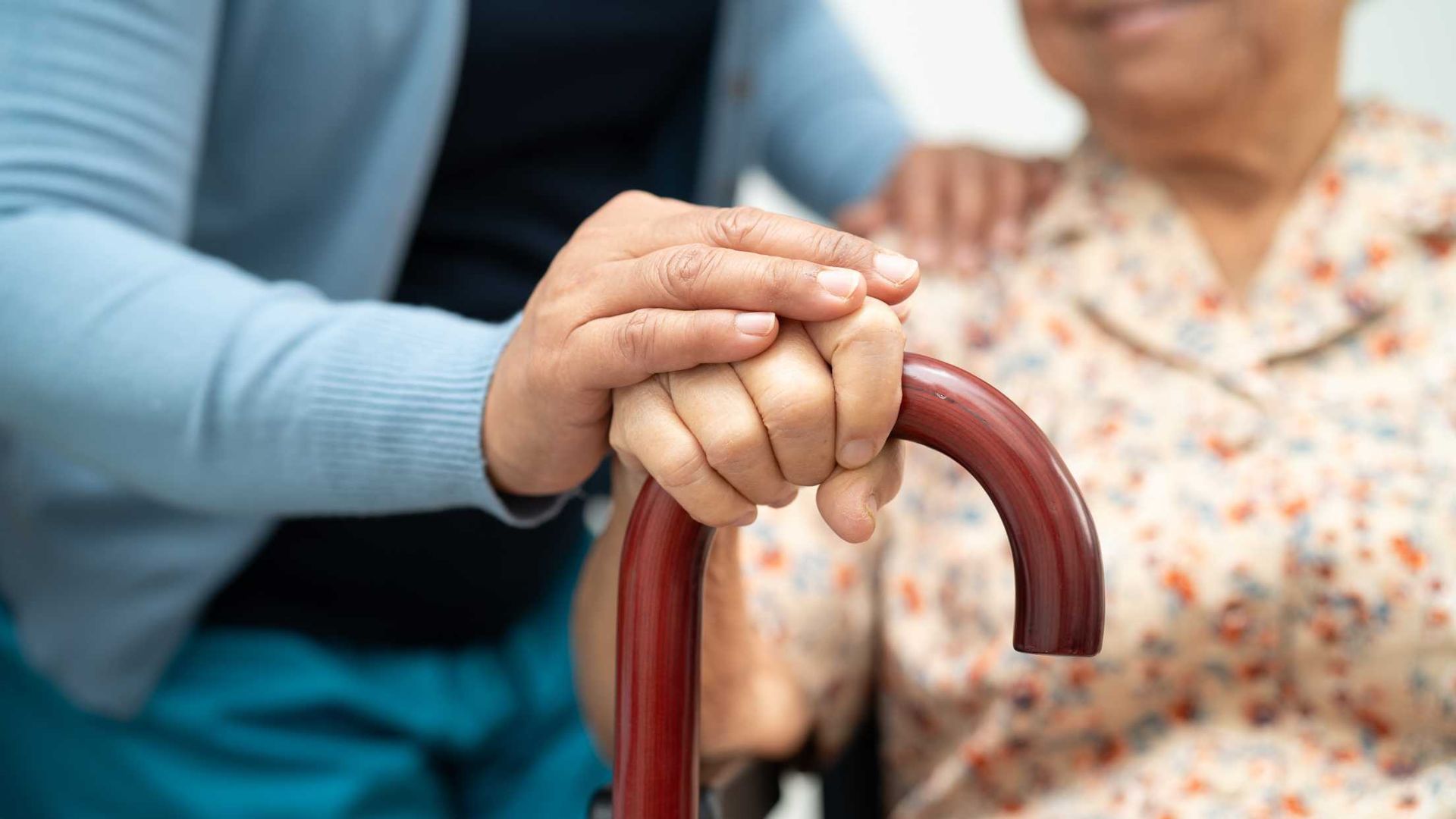 A woman is holding the hand of an elderly woman in a wheelchair.