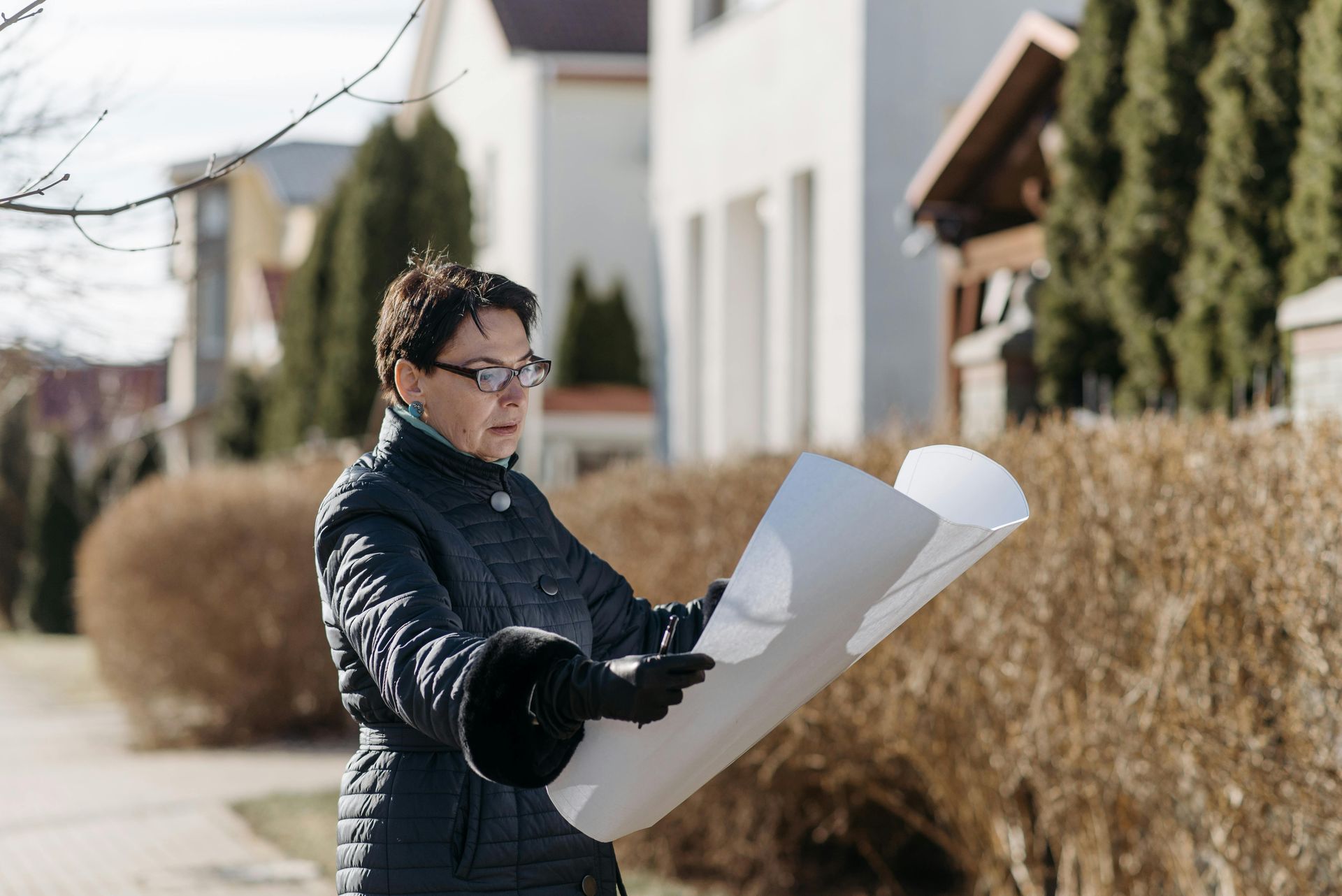 A woman is holding a large piece of paper in front of a house.