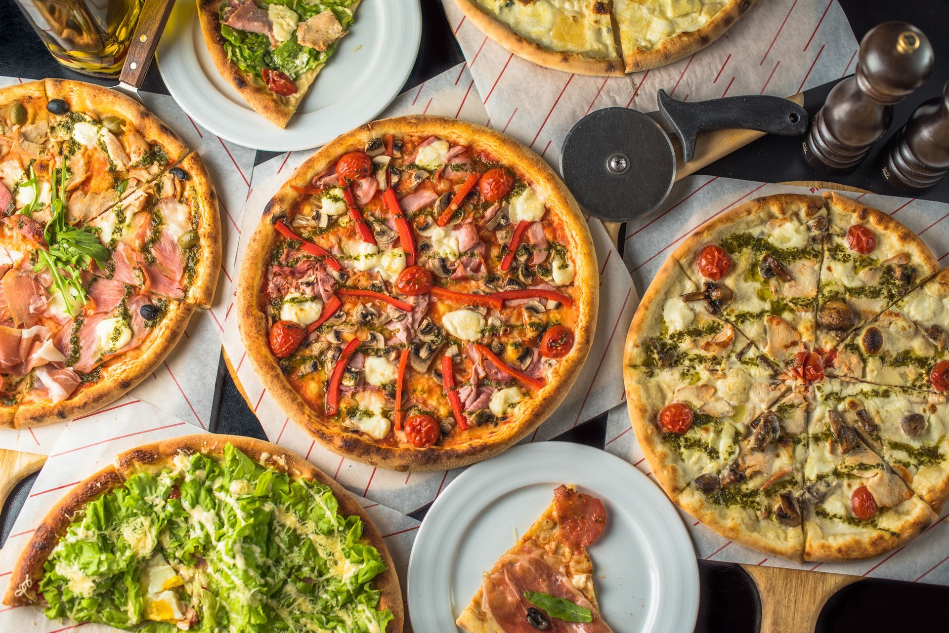 Assorted pizzas on plates, including margherita, veggie, and pepperoni, arranged on a white table.