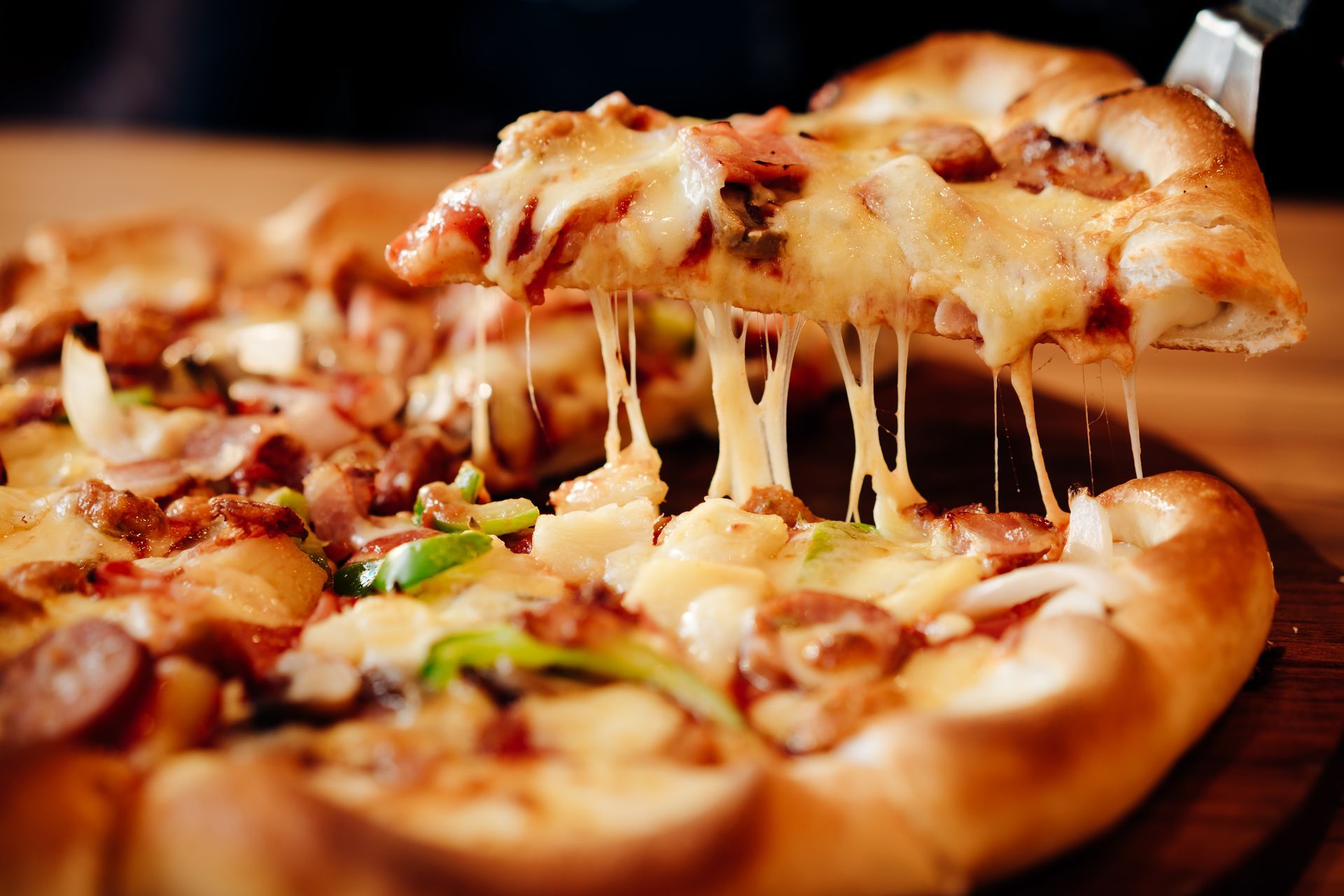 Cheesy pepperoni pizza slice being lifted, with melted cheese stretching from the pie