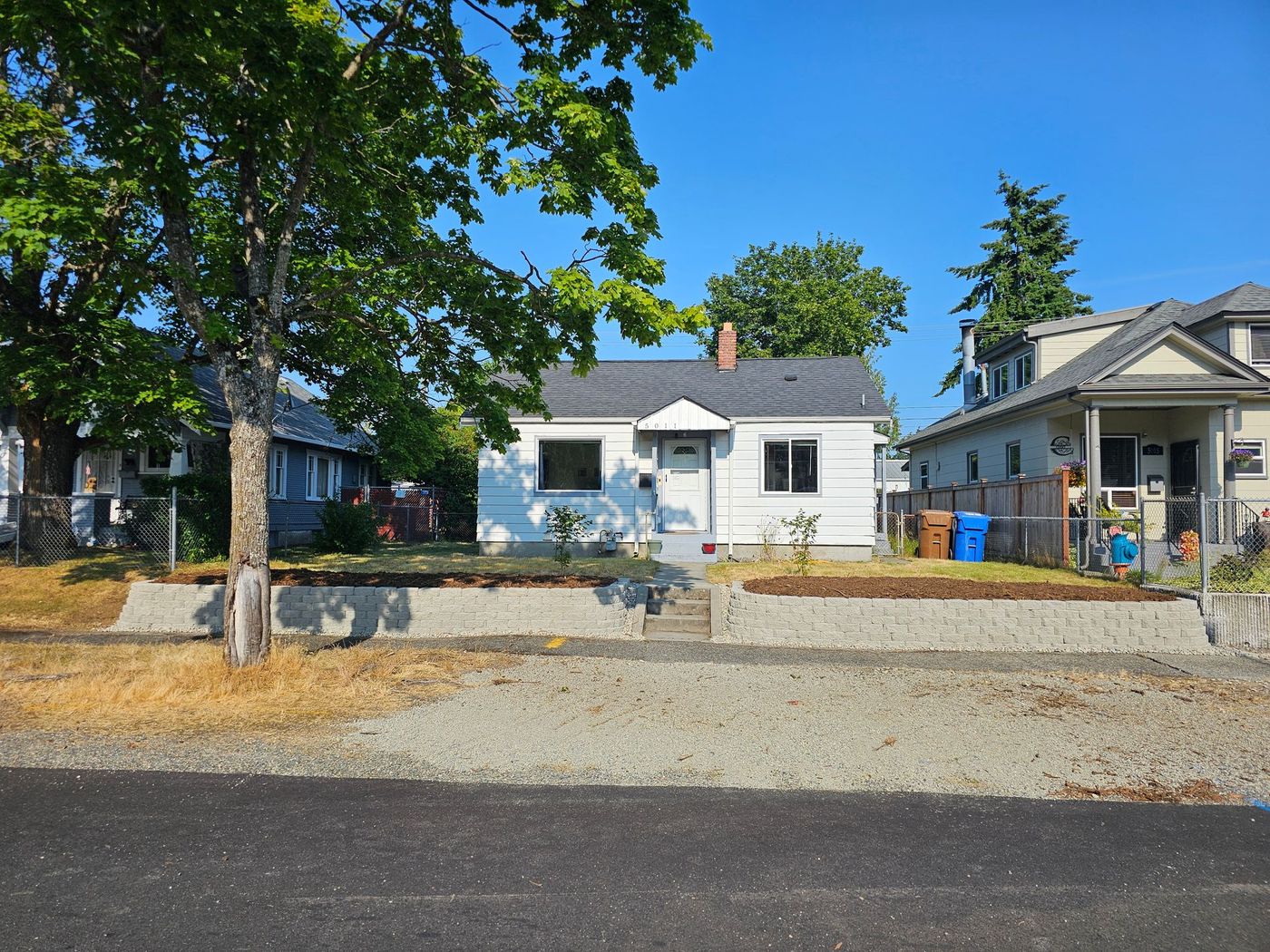 White house with gray roof, surrounded by other homes, blue sky.