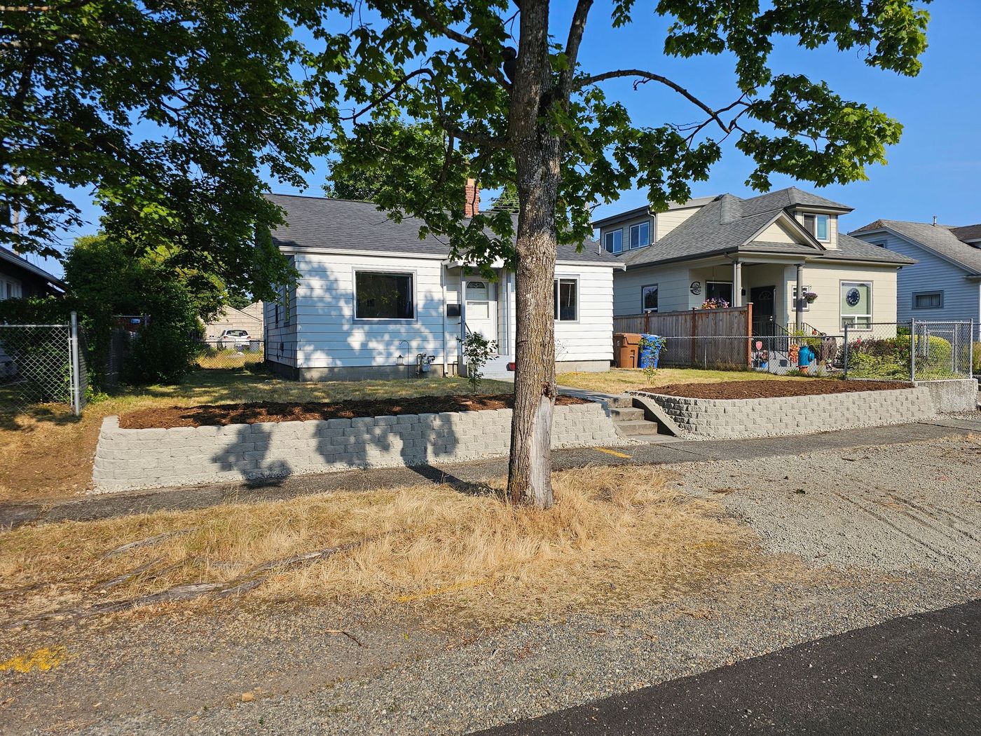 A white house behind a gray retaining wall with a tree in front.