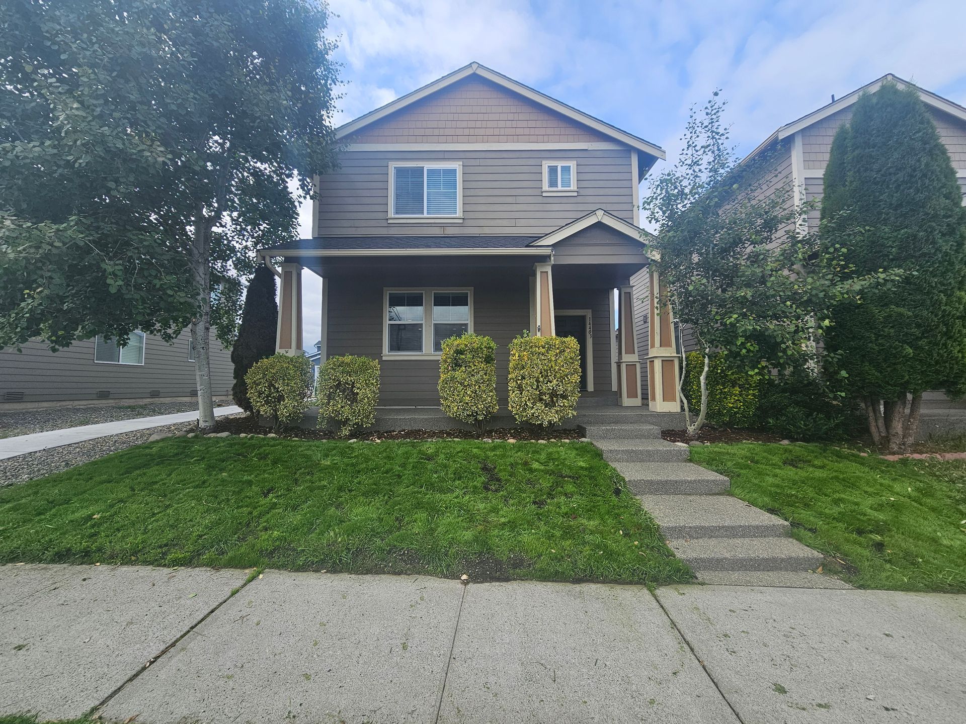 Two-story house with a green lawn, shrubs, and a concrete walkway.