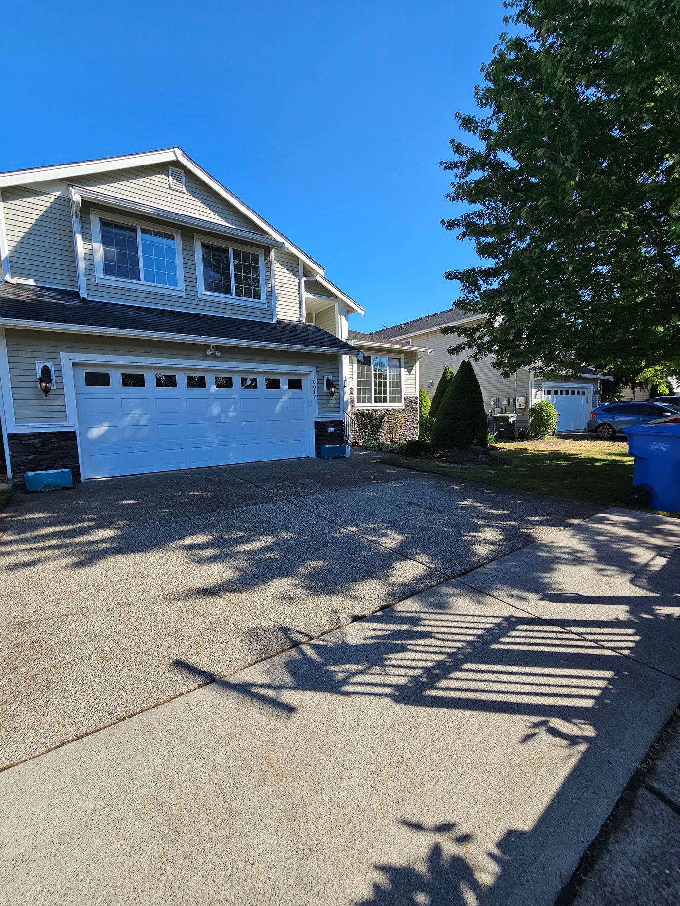 Two-story house with white garage door and gravel driveway under a bright blue sky.