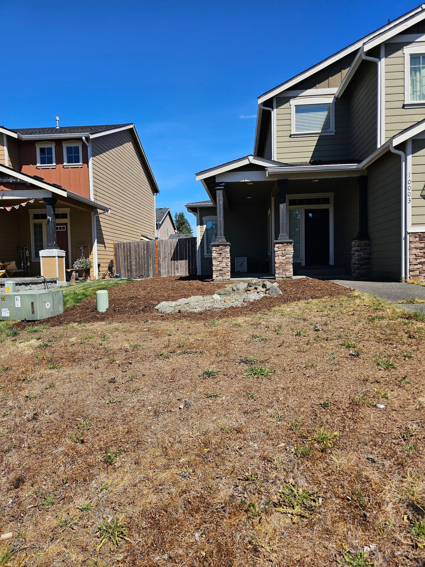 A two-story house with green siding and brown trim, set in front of a mostly dry, brown lawn.