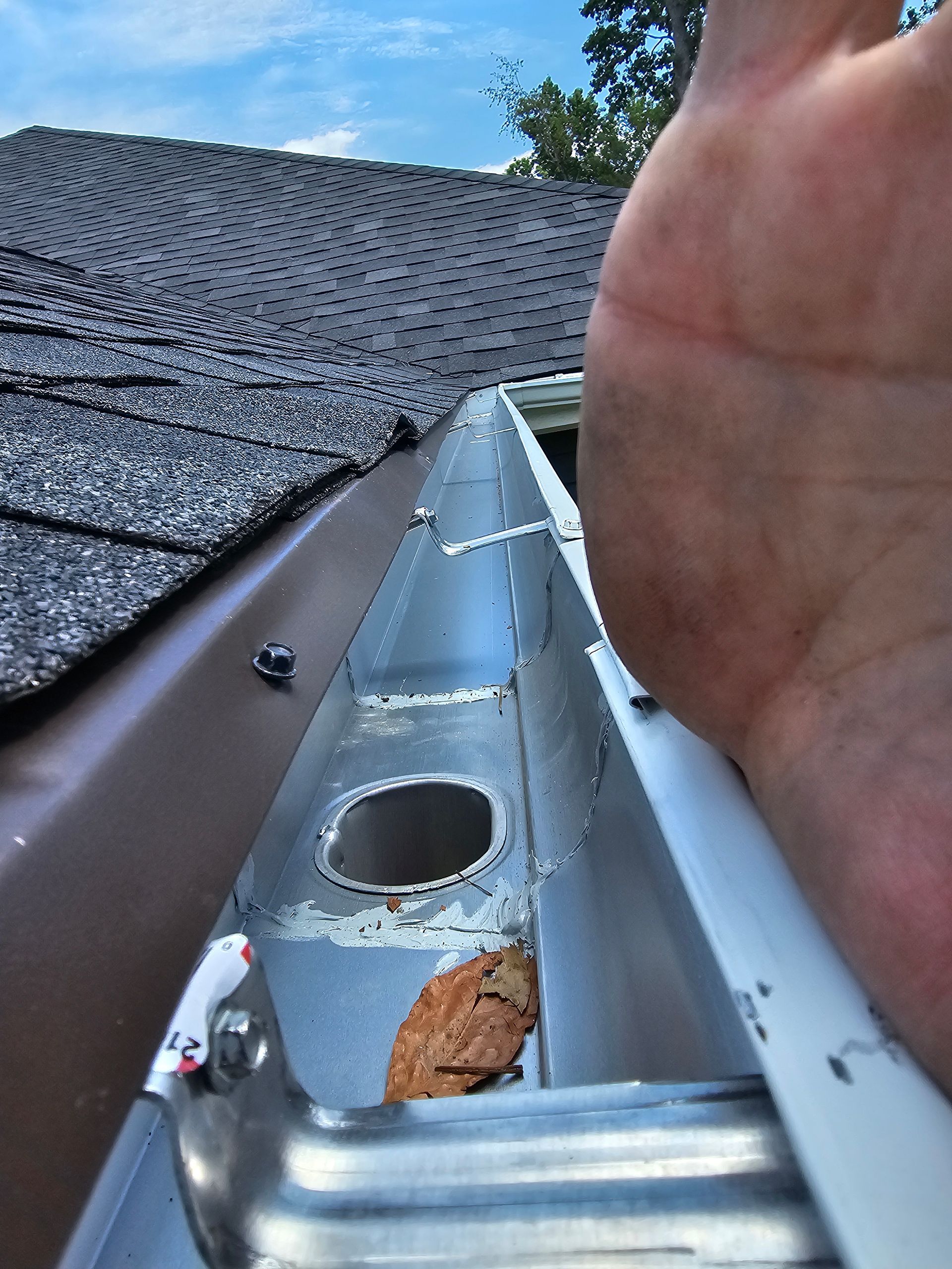 Gutter with debris and a hand reaching in, showing a close-up of the roof and the metal gutter.