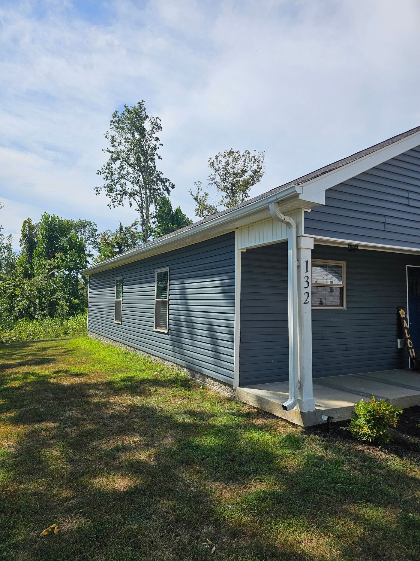 Dark gray house with white trim and address numbers, set against a blue sky and green foliage.