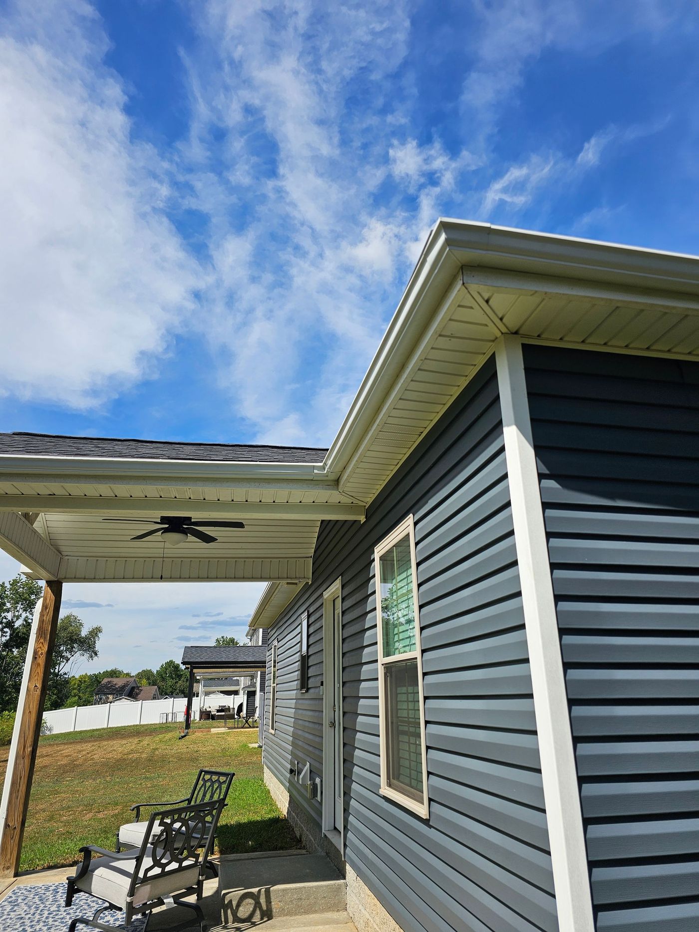 Blue-gray house exterior with white trim and light beige soffit under a cloudy blue sky.