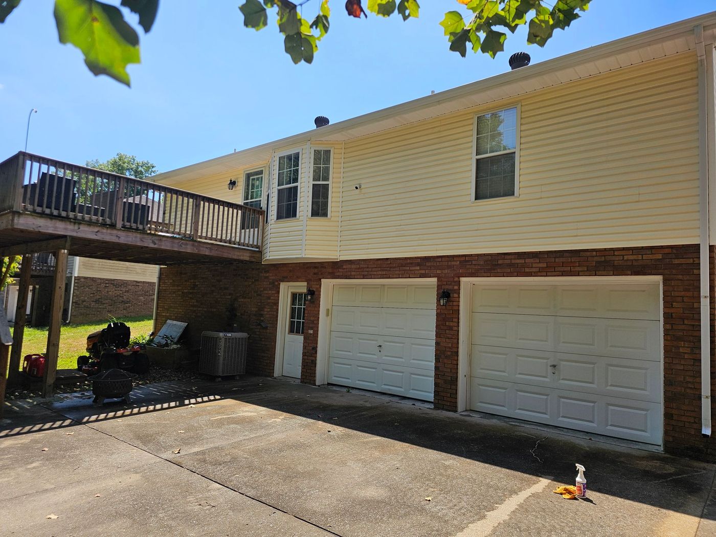 Two-story house with a deck, garage doors below. Yellow siding, brick base. Blue sky, sunny.
