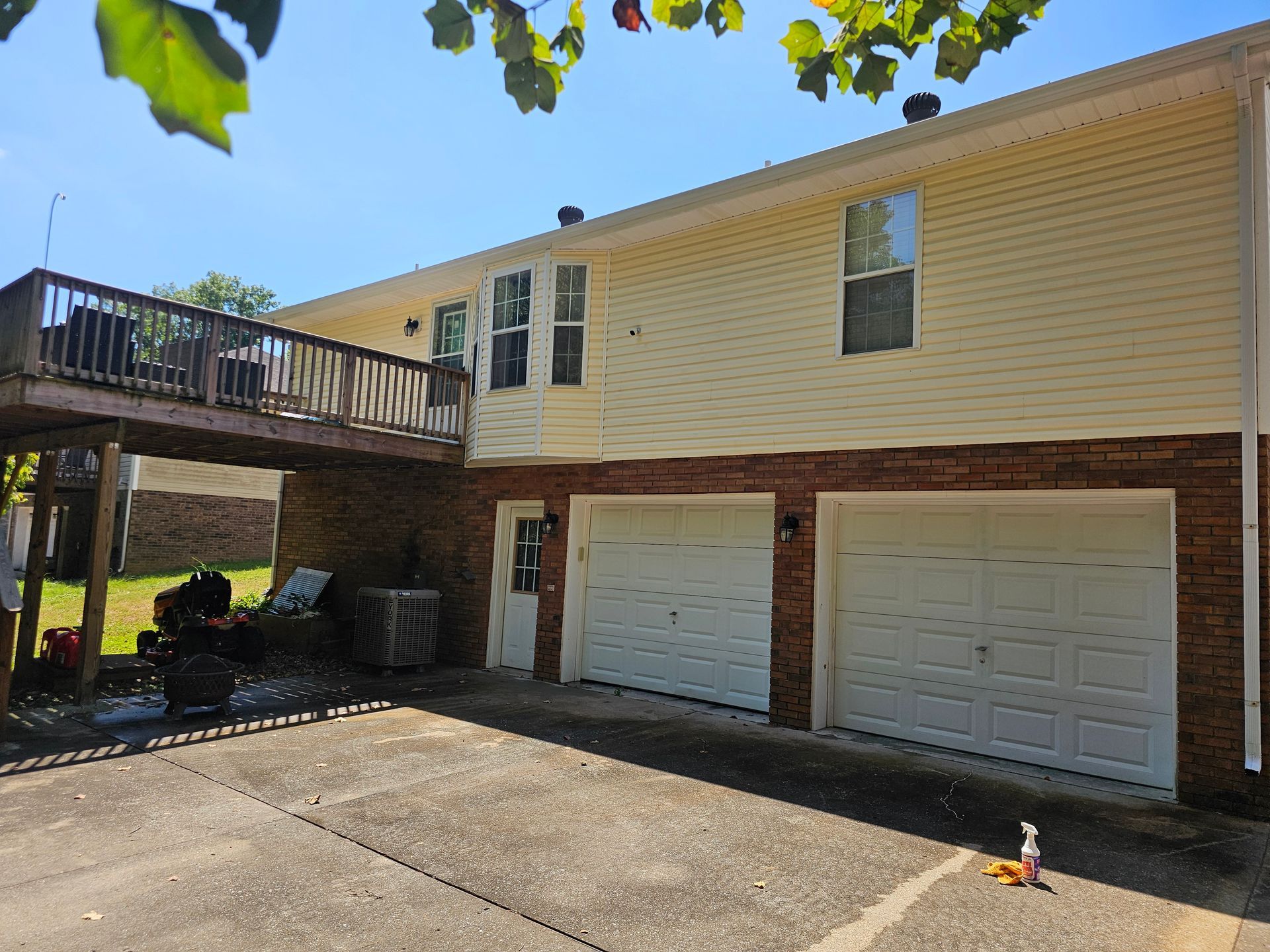 Two-story house with a deck, attached garage, and brick base. Sunny outdoor setting.