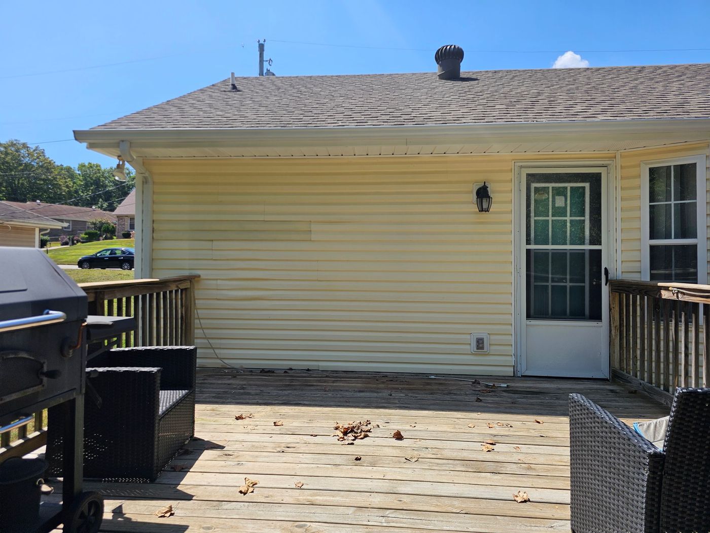 Backyard deck with yellow siding, white door, and a black grill.