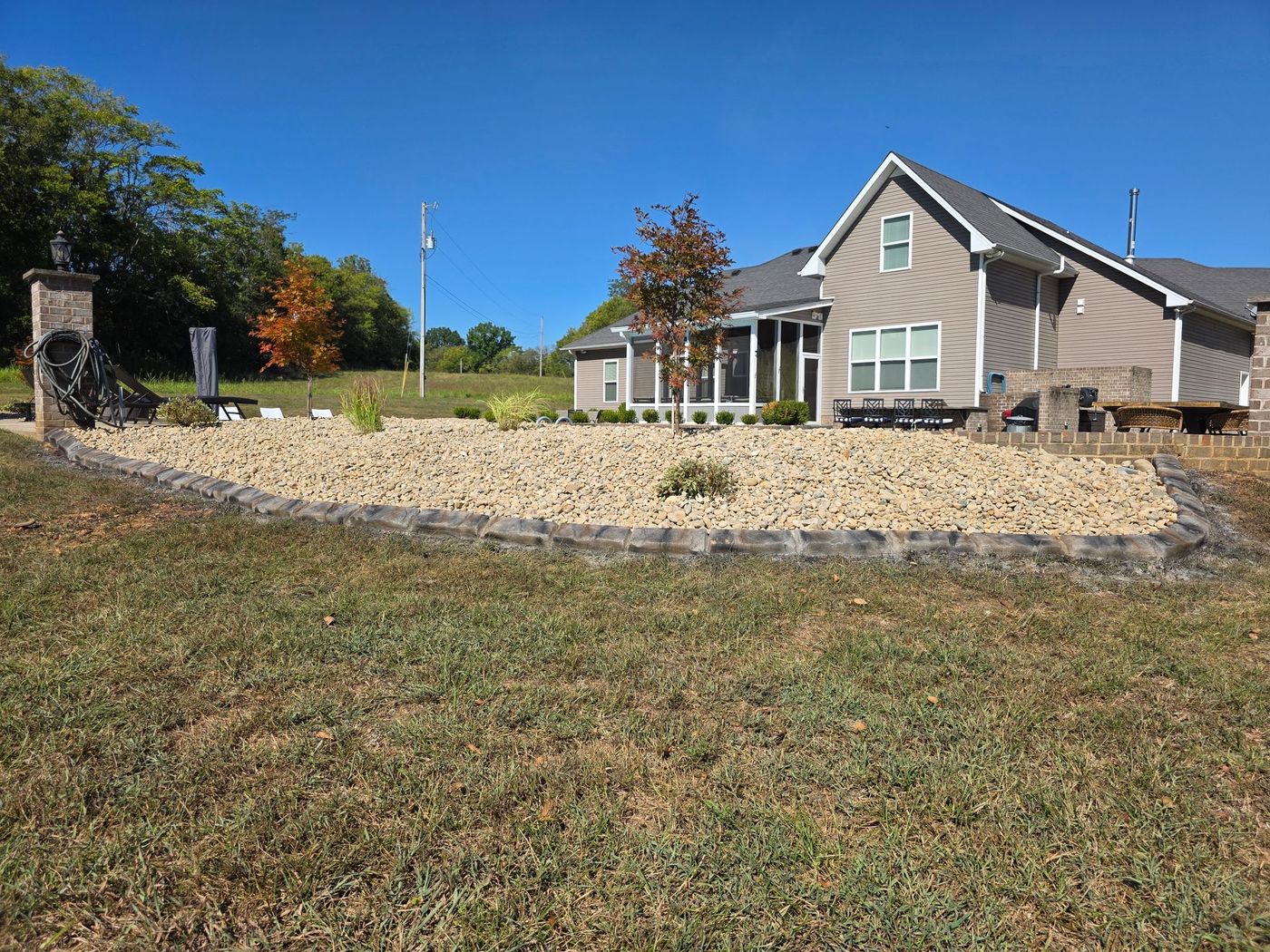 House with a rock garden in front, brown and beige colors, blue sky in background.