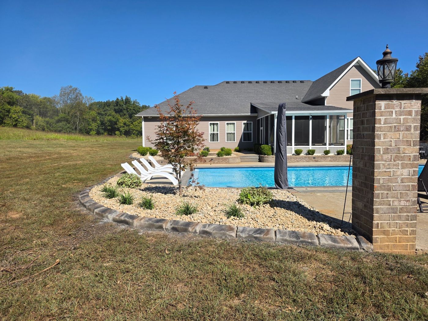 Backyard pool next to a house, with lounge chairs, landscaping, and a blue sky.