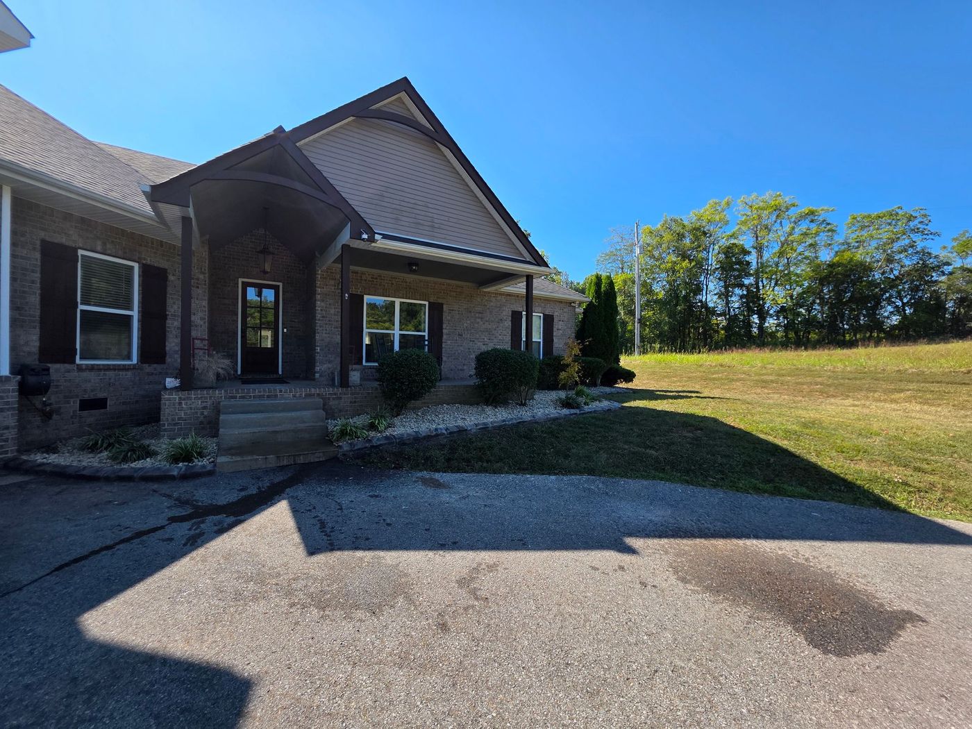 A brick home with a covered porch on a sunny day, with a green lawn and trees in the background.