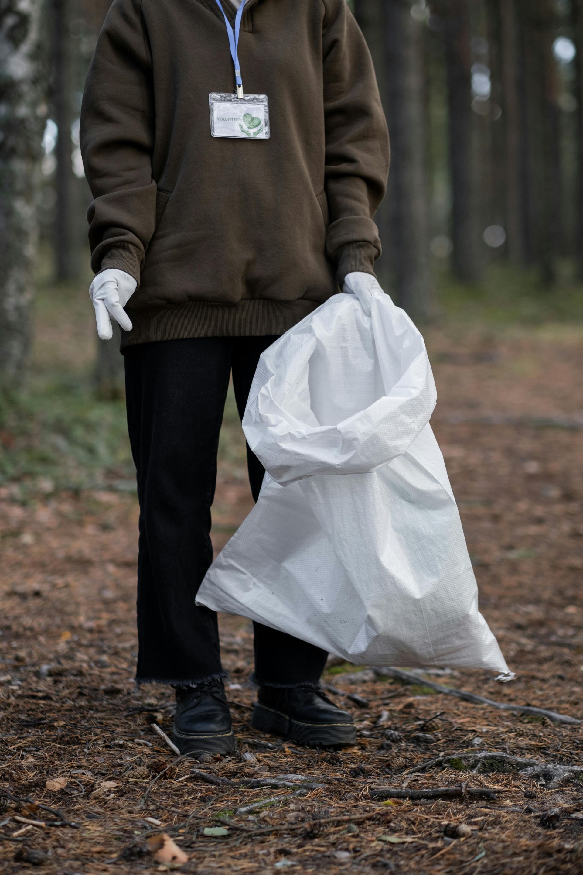 People in white hats and gloves cleaning up trash in a wooded area.